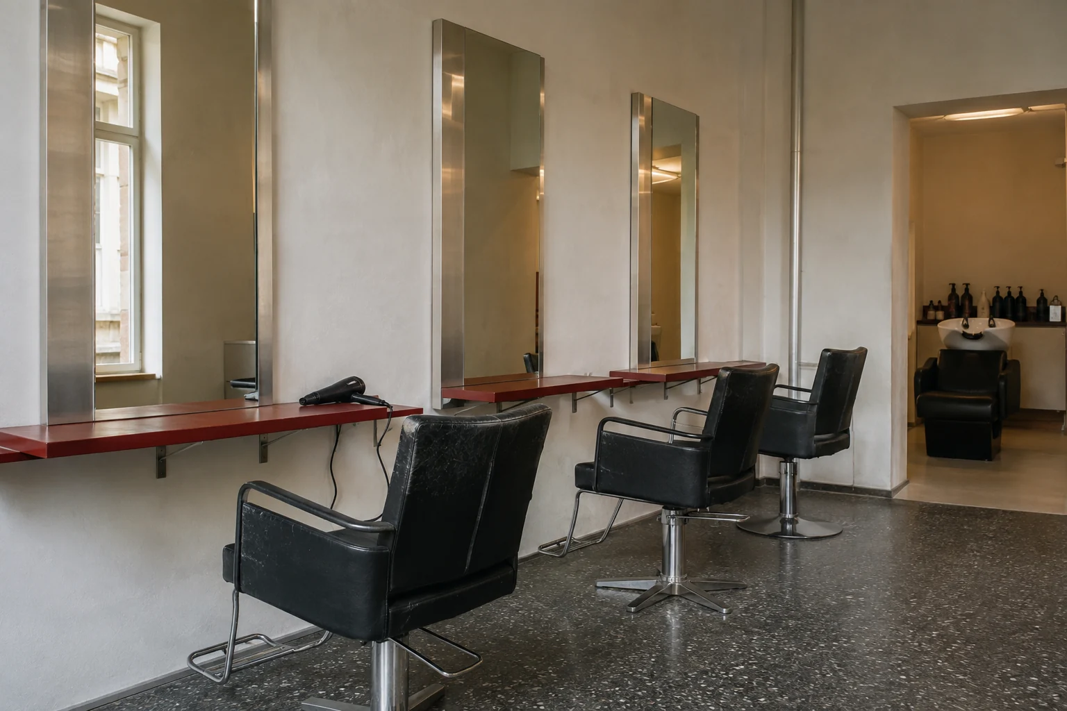 Heller Wiener Salon mit schlichten Lederstühlen, Edelstahlspiegeln und roter Ablage
